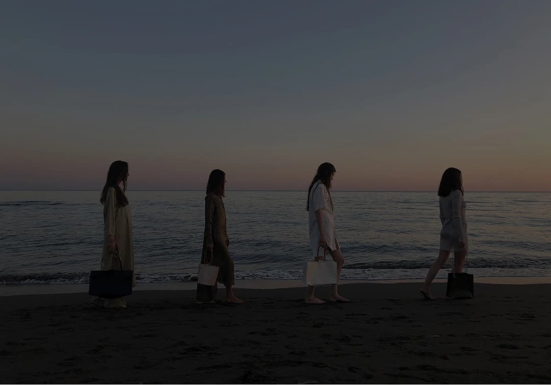 Four models walking the shoreline at dusk, carrying bags